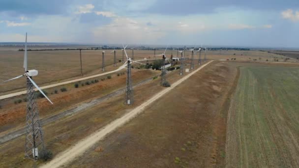 Luchtfoto van windturbines. Windturbines op de boerderij op de achtergrond van leeg veld. Rustige weersomstandigheden en windturbines werken niet zonder beweging. Paden langs de windturbines gaan in de verte — Stockvideo