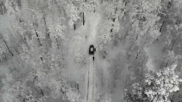 Letecký pohled na černé SUV projíždějící hlubokým bílým sněhem podél stezky v horách mezi stromy. Jeep uvízne mezi zasněženými horami, vysokými borovicemi a jedlemi. Extrémní cestování, cestovní ruch — Stock video