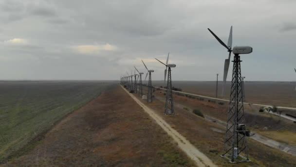 Flygfoto över vindkraftverk. Gård vindkraftverk på bakgrunden av tomt fält. Lugnt väder och vindkraftverk fungerar inte utan rörelse. Vägar längs vindturbinerna går i fjärran — Stockvideo