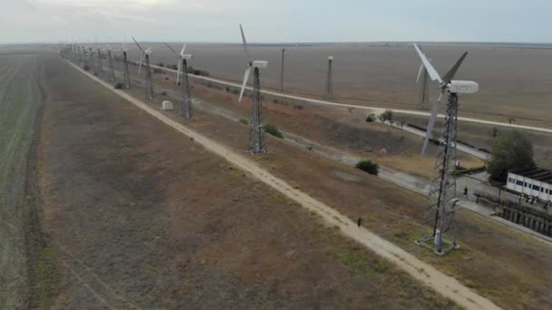 Vista aérea de los aerogeneradores. Granja de aerogeneradores en el fondo del campo vacío. Clima tranquilo y aerogeneradores no funcionan sin movimiento. Caminos a lo largo de los aerogeneradores van hacia la distancia — Vídeos de Stock