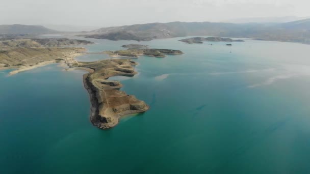 Aerial view of reservoir. Artificial lake with azure water. The mounds are like islands. There is red car on land. The clouds are reflected in the water. Mountains are visible in the distance. — Stock Video
