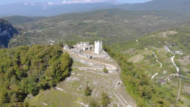 Vista aérea da torre de defesa. A fortaleza de pedra branca está localizada no topo da montanha. É iluminado pela luz solar brilhante. Você pode ver estrada serpentina e cume caucasiano na distância — Vídeo de Stock