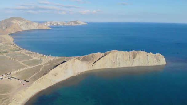 Vista aérea del Cabo Camaleón y Bahía Tranquilo, Península de Crimea. Las olas del Mar Negro se lavan sobre la colina beige del cabo. El agua lisa en la bahía tranquila está iluminada por el sol. Salida o puesta del sol — Vídeo de stock