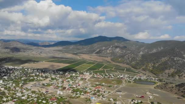 Vue aérienne de la vallée en face de la crête. Maisons colorées sont situés sur la plaine. Les champs sont divisés en places par de nombreuses routes. Il y a beaucoup de nuages dans le ciel — Video
