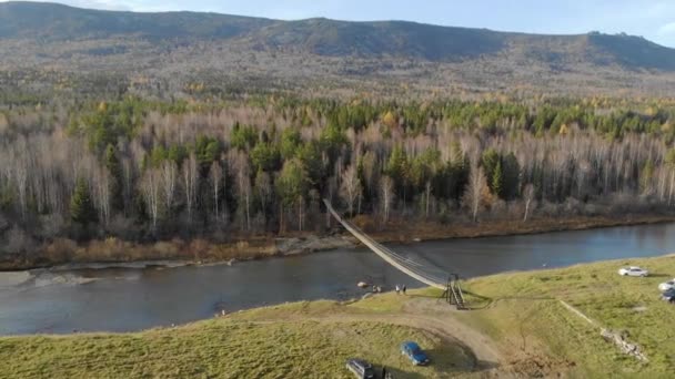 Légi kilátás a folyó feletti hídra, Dél-Urál, Oroszország. Repül a drón felett széles folyó partján, amelynek sűrű zöld növényzet. A nap süt a kék égen és a felhők mozognak. — Stock videók