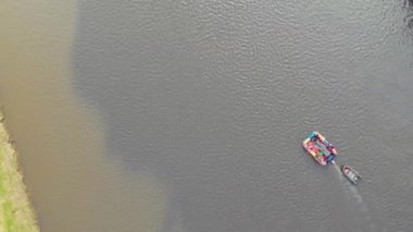 Karanlık nehrin çalkantılı akıntısı boyunca yüzen parlak şişme salın havadan görünüşü. Şişme bot sala bağlıdır. Geniş nehrin akıntısı sakin ve geniştir. Sahilde otlar büyür.