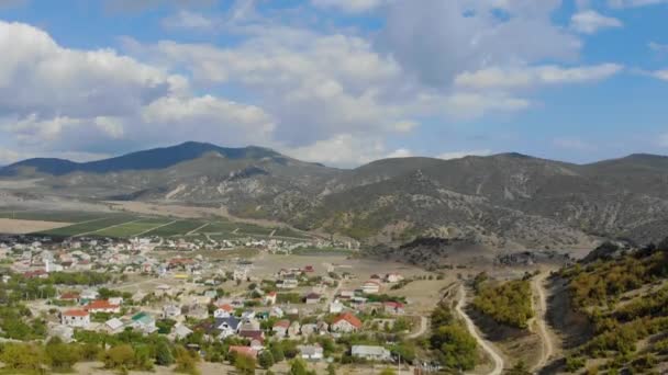 Tepenin önündeki vadinin havadan görüntüsü. Ovada renkli evler var. Tarlalar birçok yola göre meydanlara ayrılır. Gökyüzünde bir sürü bulut var. — Stok video