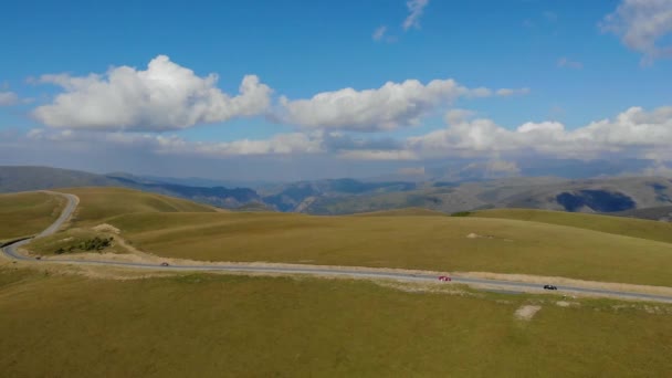 Luchtfoto van de weg langs de Kaukasus, Elbrus. Auto 's staan op de weg tussen groene weiden. De zon verlicht de toppen van de bergen — Stockvideo