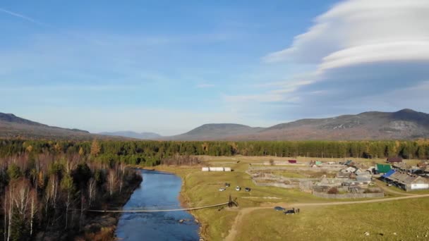 Αεροφωτογραφία της πεζογέφυρας πάνω από το ποτάμι, South Ural, Ρωσία. Πετώντας σε drone πάνω από ευρύ ποτάμι στις όχθες του οποίου πυκνή πράσινη βλάστηση. Ο ήλιος λάμπει στον γαλάζιο ουρανό και τα σύννεφα κινούνται — Αρχείο Βίντεο