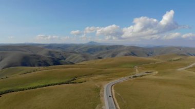 Kafkaslar 'ın Elbrus bölgesindeki dağ sırasından geçen yolun havadan görünüşü. Yeşil çayırların arasında arabalar yolda duruyor. Güneş dağların zirvelerini aydınlatır.