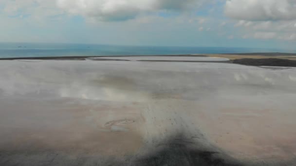 Вид с воздуха на бежевое соленое озеро. Озеро это зеркало. Вода озера отражает голубое небо и плавающие облака. Озеро и море разделены песком. Видно синее спокойное море — стоковое видео