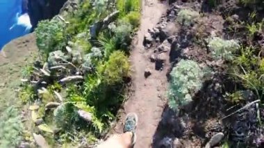 Adam dağın tepesine tırmanıyor ve patika boyunca yürüyor. Deniz koyunun yukarısındaki dağın kenarından geçiyor. Mavi okyanus, yoğun yeşillikler arasında görülebilen kayalara çarpar. Hafif bir esinti. Yürüyüş