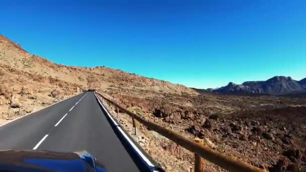 L'auto guida su strada pianeggiante attraverso il deserto. Le colline sono visibili in lontananza. Non c'è vegetazione. Strada con segni bianchi, cartelli, recinzioni. Tempo soleggiato, cielo azzurro. Sparatoria da parte di auto azzurra — Video Stock