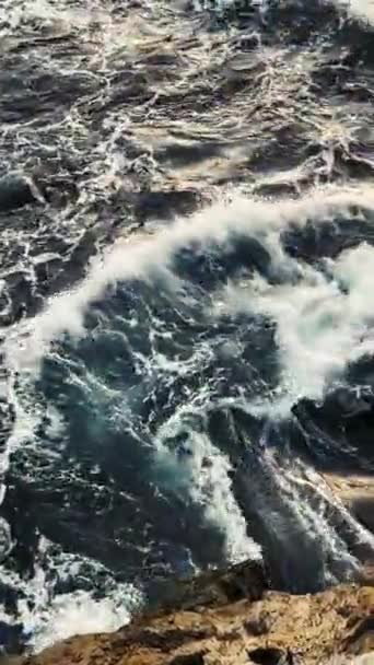 Vernietigende en indrukwekkende golven. Zeestorm. Golven crashen tegen kustrotsen, wat een explosie van water veroorzaakt. Bovenaanzicht van gigantische oceaangolven die neerstorten en schuimen op het strand met rotsen. Verticale video — Stockvideo