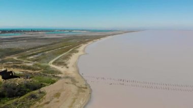 Pembe ıssız tuz gölü, Kırım Yarımadası 'nın havadan görünüşü. Uzakta, tahta kütüklerden oluşan bir patika suya giriyor. Göl ve deniz kumlu bir şeritle ayrılır. Eşsiz doğa.