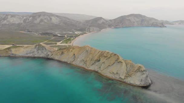 Aerial view of Cape Chameleon and Quiet Bay, Crimean Peninsula. Waves of the Black Sea wash over the beige hill of the cape. Smooth water in Quiet Bay is illuminated by sun. Sunrise or sunset — Stock Video