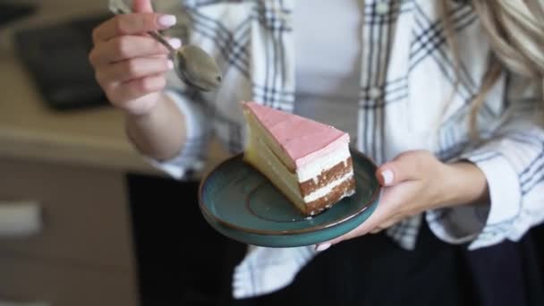 Вкусный торт на тарелке, ложка отрывает кусочек. Домохозяйка с светлыми волосами ест вкусный торт на кухне, девушка пробует торт на блюдце дома в свой день рождения — стоковое видео