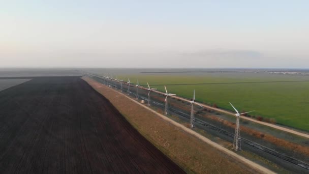 Flygfoto över vindkraftverk. Gård vindkraftverk på bakgrunden av tomt fält. Lugnt väder och vindkraftverk fungerar inte utan rörelse. Vägar längs vindturbinerna går i fjärran — Stockvideo
