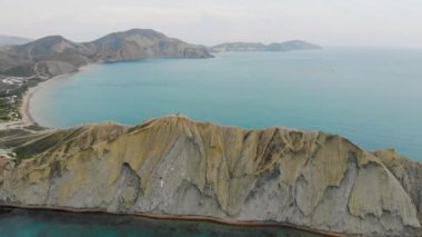 Cape Chameleon ve Quiet Bay, Kırım Yarımadası 'nın hava manzarası. Karadeniz 'in dalgaları pelerinin bej rengi tepenin üzerinde süzülüyor. Sessiz Körfez 'deki pürüzsüz su güneşle aydınlanır. Gün doğumu ya da gün batımı