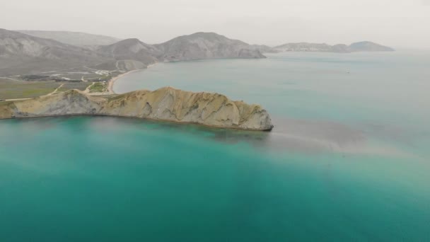 Vista aérea de Cape Chameleon e Quiet Bay, Península da Crimeia. Ondas do Mar Negro se lavam sobre a colina bege da capa. A água suave em Quiet Bay é iluminada pelo sol. Nascer ou pôr-do-sol — Vídeo de Stock