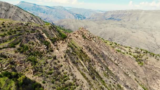 Vista aérea de Gamsutl, Cáucaso. Antiguos edificios destruidos se encuentran en la cima de la montaña. Detrás se pueden ver enormes pendientes de capas de cresta. Impresionante vista contra el telón de fondo del cielo brillante con nubes — Vídeos de Stock