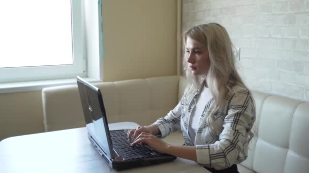 Mujer trabaja detrás de la computadora portátil en la cocina — Vídeos de Stock