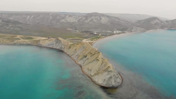 Aerial view of Cape Chameleon and Quiet Bay, Crimean Peninsula. Waves of the Black Sea wash over the beige hill of the cape. Smooth water in Quiet Bay is illuminated by sun. Sunrise or sunset — Stock Video