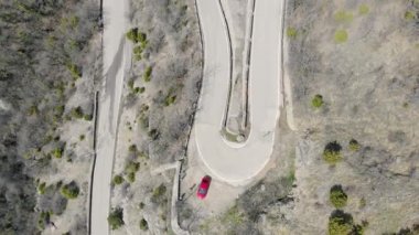 Dağlarda yılanlı yol. Arabalar dağın zirvesine giden yolda ilerliyorlar. Yolun kenarlarında gri kayalar ve küçük bitkiler var.