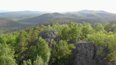 Dağın tepesindeki yeşil ağaçların havadan görünüşü. Güneş, çamların ve köknar ağaçlarının parlak yoğun yeşilliğini aydınlatır. Dağın zirvesi ağaçlar arasında görülebilir. Gün doğumu ya da gün batımı