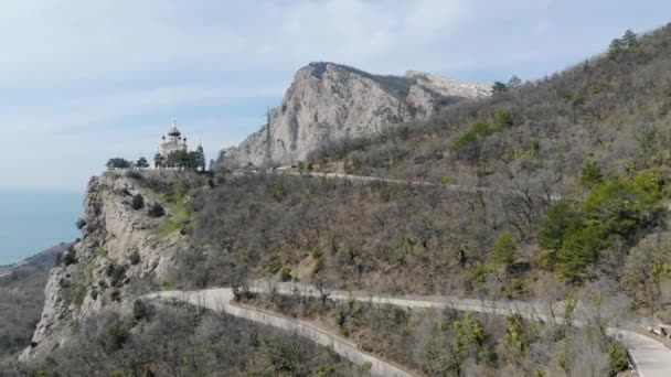 Fehér falú szent templom zöld kupolákkal a hegy tetején, Krími-félszigeten. Az autók a szerpentin úton haladnak a templomhoz. Kilátás a tengerre és a városra a hegy alatt — Stock videók