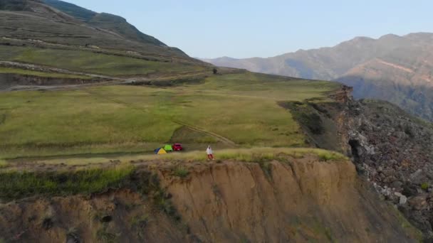 Повітряний вид туристів, які прокидаються і зустрічаються зі сходом сонця на скелі в Дагестані. Червоний автомобіль і намети на тлі високих гір. Гірська долина і зелень на гірському хребті Кавказу. — стокове відео