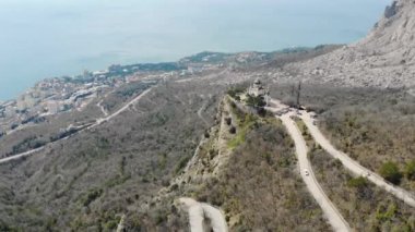 Dağın tepesinde Kırım Yarımadası 'nın yeşil kubbeleri olan beyaz duvarlı kutsal kilise. Arabalar sinagoga doğru serpentine yolu boyunca gidiyor. Dağların altında deniz ve şehir manzarası