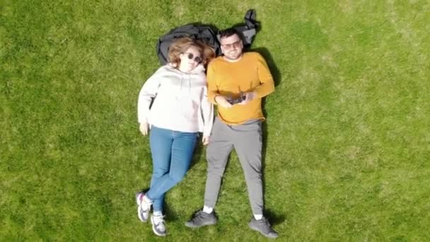 Vista aérea de un moderno parque de recreo. Una pareja enamorada se encuentra en un césped verde entre árboles y plantas únicas. Parque Galitsky — Vídeos de Stock