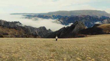 Kafkas Dağları 'nın havadan görünüşü. Kadın sahada durup gülümsüyor. Gri gökyüzü yeşil çayırların üzerinde görünür. Beyaz bulutlar nehri oluşturur. Bulutlu hava
