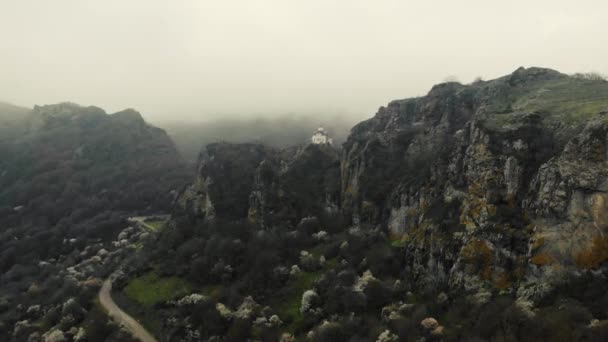 Вид на стародавній храм на вершині гори. Білі стіни споруди видно на вершині гори серед яскраво-зелених дерев. Густі хмари і туман спускаються. Похмура погода — стокове відео