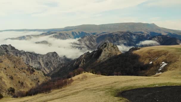Luftaufnahme des Kaukasus-Gebirges. Grauer Himmel ist über grünen Wiesen zu sehen. Weiße Wolken bilden einen Fluss. Gipfel scharfer Berge sind mit Gletschern bedeckt und in der Ferne liegt Schnee. Bewölktes Wetter — Stockvideo