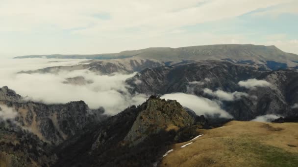 Vista aérea de las montañas del Cáucaso. El cielo gris es visible sobre prados verdes. Nubes blancas forman el río. Picos de montañas afiladas están cubiertas de glaciares y nieve en la distancia. Clima nublado — Vídeo de stock