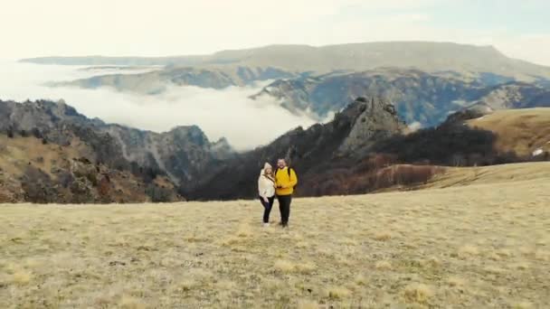 Vista aérea de las montañas del Cáucaso. Un par de personas están de pie en el campo. El cielo gris es visible sobre prados verdes. Nubes blancas forman el río. Clima nublado — Vídeos de Stock
