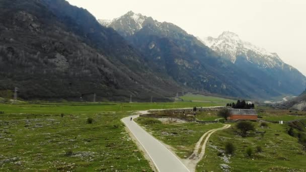 Flygfoto över dalen genom vilken bergsfloden rinner. Valley är täckt av grönska. Du kan se snöiga bergstoppar. Motorvägen passerar genom ängen och husen är synliga — Stockvideo