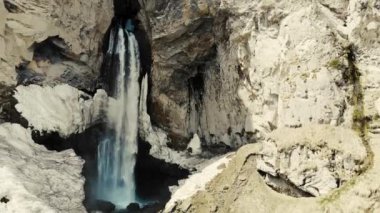 Elbrus bölgesindeki dağ şelalesinin havadan görünüşü. Fırtınalı nehir dağın tepesinden aşağı akıyor. Nehir yerde kırılır. Kafkas dağlarının yüksek tepelerini görebilirsiniz. Karla kaplı.