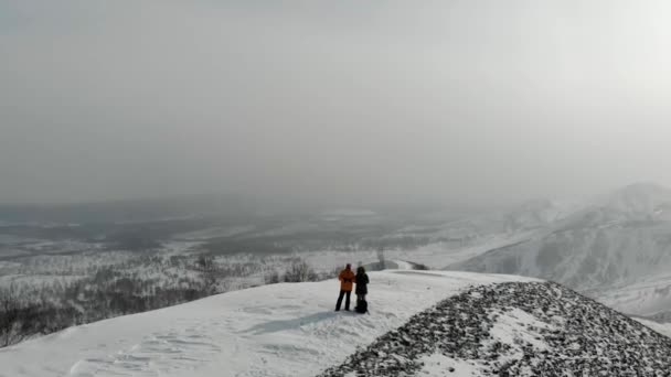 Légi felvétel a vaskeresztről és az emberekről, akik a hegy tetején állnak. A gyár hátulról látható. A téli hegyeket kissé beborítja a hó. Környezetszennyezés. Ártalmas termelés, mérgezés — Stock videók