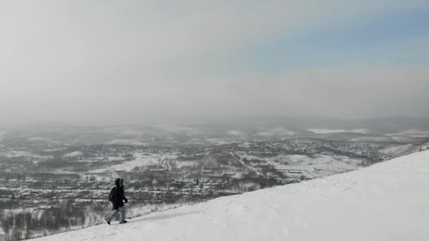 Aerial view of mountain path that woman is walking up. Road is covered with snow. Small winter hills around. Trees are visible. There are gray skies and clouds all around. Beautiful gloomy view — Stock Video