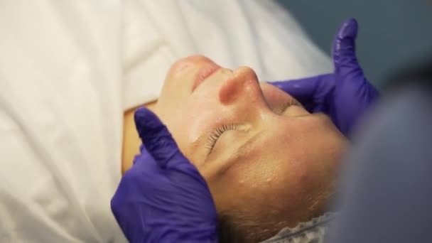 El médico aplica compuesto curativo para el acné con movimientos de palmaditas en la cara brillante de las mujeres. Cosmetólogo ha aplicado máscara y está haciendo masaje facial. Manos en guantes. Tratamiento del acné. Masaje facial — Vídeo de stock