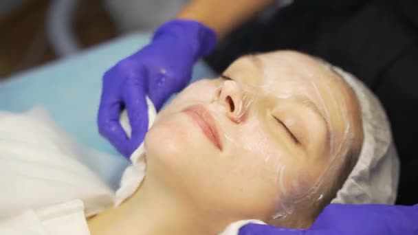 Cosmetologist traite les femmes visage avec des éponges blanches. Nettoyer la peau des impuretés. Rendez-vous chez le médecin. Cap est mis sur ses cheveux, gants lilas sont sur les mains des médecins. Peau blanche et propre — Video