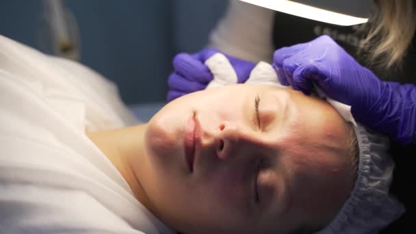 Lekarz wyciska pryszcze na twarz kobiety. Ręce w rękawiczkach trzymają sterylne gąbki i usuwają brud i pryszcze na jasną skórę pacjenta. Procedura oczyszczania skóry — Wideo stockowe