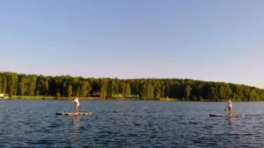 İki arkadaş göl kıyısından sorunsuzca uzaklaşıp kürek çekiyorlar. Yeşil ağaçlar kıyıda yetişir. Gün batımı ya da gün doğumu uzaktan görülebilir. Rüzgar yavaşça suyu karıştırır. Hava görünümü