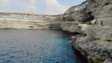 Dik kayadaki mağaranın havadan görünüşü, Cape Tarkhankut, Kırım Yarımadası. Gök mavisi berrak deniz. İnsanlarla dolu bir tekne mağarada yüzüyor. Kadın uçurumdan suya atlıyor. Ekstrem eğlence