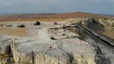 Beyaz Kaya 'nın havadan görünüşü, Kırım Yarımadası. Kadın ve erkek yüksek uçurumun kenarında dikiliyorlar. Turistler kayalık plato boyunca yürürler. Dağ bulutlu gökyüzüne karşı parlak görünüyor. Turizm