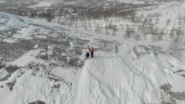 Couple of people are standing on hill. Man and woman are standing on top of snow-covered hill. They stopped to rest. Man in yellow jacket waves his hand. Snow slopes and trees can be seen. Aerial view — Stock Video