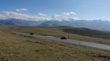 Kafkaslar 'ın Elbrus bölgesindeki dağ sırasından geçen yolun havadan görünüşü. Yeşil çayırların arasında arabalar yolda duruyor. Güneş dağların zirvelerini aydınlatır.